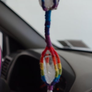 Könnte beinhalten: Ein Regenbogenfarbener Makramee-Anhänger mit einem klaren Kristall in der Mitte. Der Anhänger ist aus verschiedenen bunten Fäden gefertigt und in einem Knotenmuster gebunden.