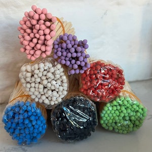May include: Assortment of colorful matchsticks bundled together. The matchsticks are arranged in a circle with the tips of the matches facing outward. The colors of the matchsticks are pink, purple, white, red, black, and green.