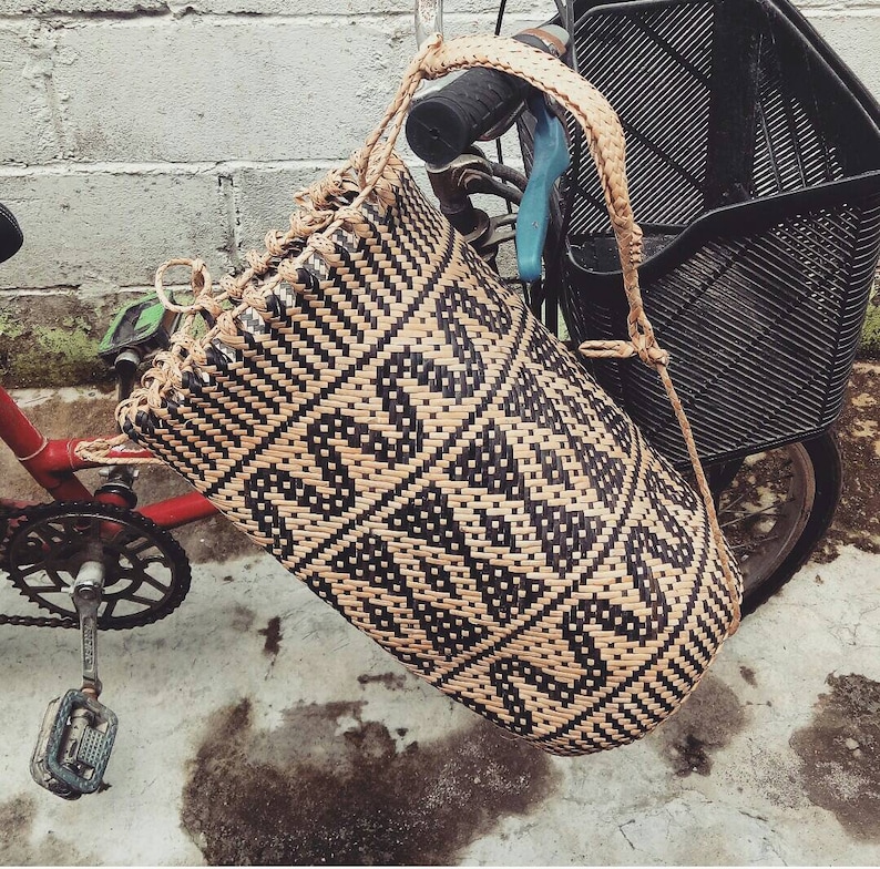 May include: A black and tan woven basket bag with a geometric pattern hangs from a bicycle.
