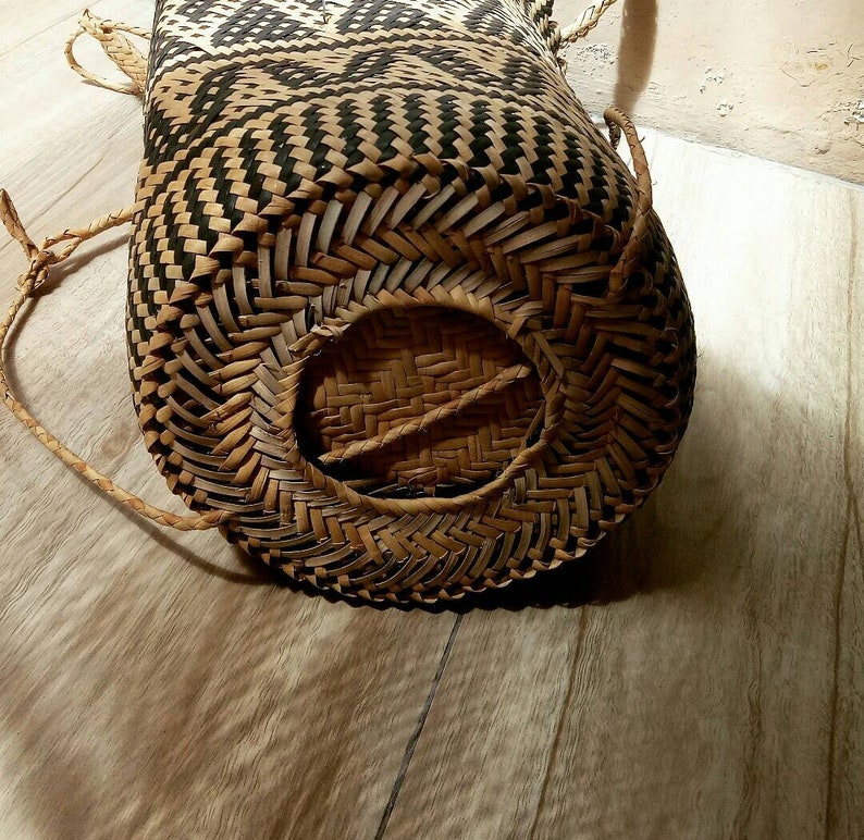 May include: A woven basket with a black and white pattern and a round opening on the bottom. The basket is made of natural materials and has a rustic look.