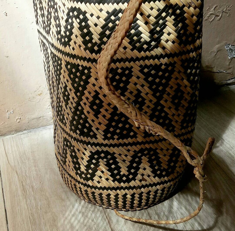 May include: A woven basket with a black and brown geometric pattern. The basket has a long, woven handle.