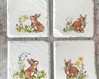 May include: Set of four white square coasters with a brown bunny rabbit and floral design. Each coaster features a different bunny rabbit pose and floral arrangement.