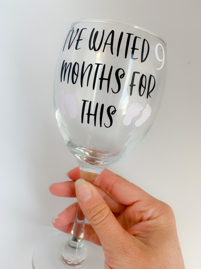 May include: A clear glass wine glass with the text "I've waited 9 months for this" and two white baby footprints on the side.