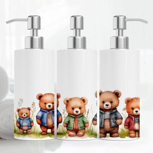 May include: Three white ceramic soap dispensers with stainless steel pumps. Each dispenser features a different cartoon bear design. The bears are wearing different colored clothing. The bears are standing in front of a green background with white flowers.