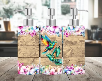 May include: Three decorative soap dispensers with silver pumps. Each dispenser features a wooden background with a watercolor design of colorful flowers and hummingbirds. The flowers are pink, purple, and blue.