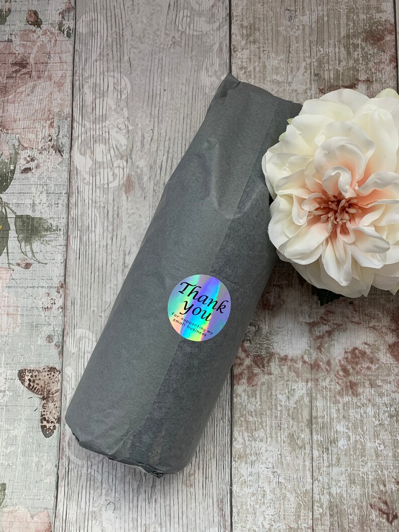 May include: A gray gift bag with a holographic sticker that says "Thank you for supporting my small business". The bag is on a wooden surface with a white flower.