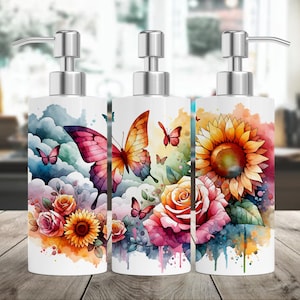 May include: Three white ceramic soap dispensers with silver pumps. Each dispenser features a different watercolor design: a butterfly with pink and yellow wings, a sunflower with yellow petals, and a pink rose with green leaves.