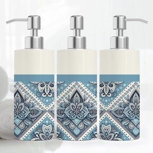 May include: Three decorative soap dispensers with a cream-colored top and a blue and white patterned design. The dispensers have silver-colored pump tops and are arranged in a row. Rolled white towels are visible in the background.