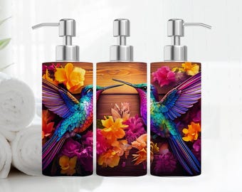 May include: Three clear glass bottles with silver pumps and colorful hummingbird designs. The bottles are filled with liquid soap and have a wooden background.