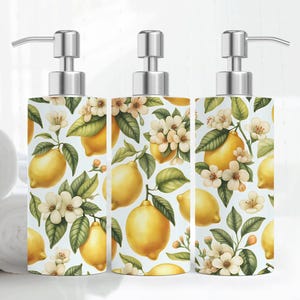 May include: Three decorative soap dispensers with a stainless steel pump. The dispensers feature a white background with a pattern of yellow lemons, green leaves, and white flowers. The dispensers are cylindrical in shape.