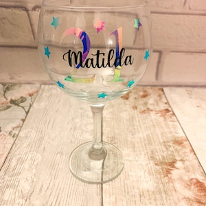 Könnte beinhalten: Ein klares Glas-Gin-Glas mit einem regenbogenfarbenen, schimmernden Aufkleber, auf dem "21 Matilda" steht, und blauen Stern-Aufklebern.