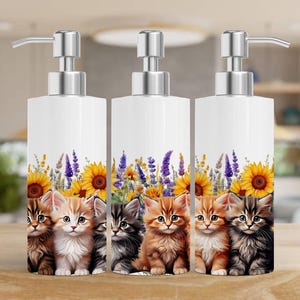 May include: Three white soap dispensers with silver pumps and floral designs. Each dispenser features a row of three adorable kittens with sunflowers and lavender.