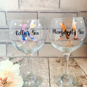 May include: Two clear glass gin glasses with personalized names and gold and iridescent glitter stars. The glasses say "Kelly's Gin" and "Margaret's Gin".