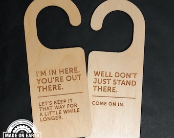Puede incluir: Dos colgadores de puerta de madera con un mensaje humorístico. El colgador de la izquierda dice "Estoy aquí. Tú estás ahí fuera. Mantengamos las cosas así un poco más tiempo." El colgador de la derecha dice "Bueno, no te quedes ahí parado. Entra."