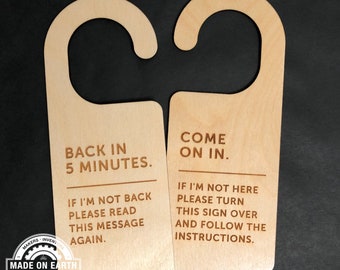 Puede incluir: Dos colgadores de puerta de madera con texto. El primer colgador dice "Back in 5 minutes. If I'm not back please read this message again." El segundo colgador dice "Come on in. If I'm not here please turn this sign over and follow the instructions."
