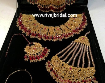 May include: A gold bridal jewellery set with red and clear beads. The set includes a necklace, earrings, a maang tikka, a nose ring, and a long necklace with a decorative top.