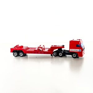 May include: A red toy truck with a flatbed trailer. The truck has "Royal Air Force" written on the side. The trailer is empty.