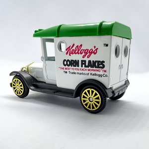 Op de afbeelding: Een witte speelgoed-bezorgwagen met een groen dak en gele wielen. De wagen heeft een Kellogg's Corn Flakes logo aan de zijkant met de slogan "Het beste voor u elke ochtend".