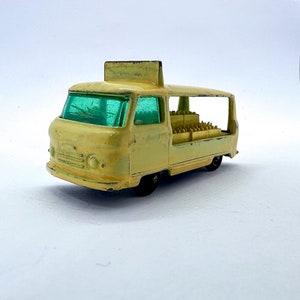 May include: A yellow toy van with a green windshield and a sign on top. The van is carrying a load of small, rectangular boxes.