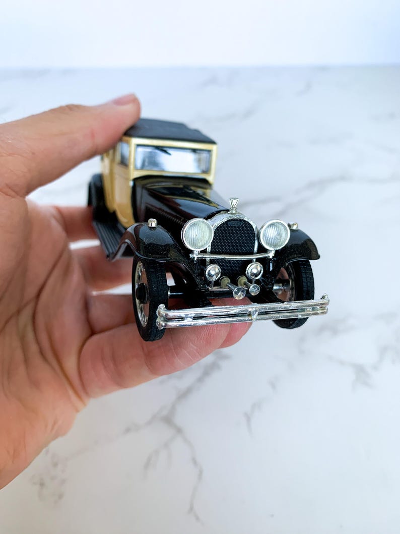 May include: A black and gold toy car model with a detailed front grill and headlights. The car has a black body and a gold roof.