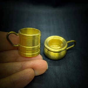 May include: Two miniature gold-colored metal containers. One is a mug with a handle and the other is a small pot with a handle.