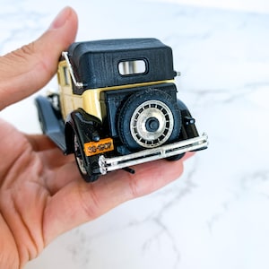 May include: A black and cream toy car model with a black convertible top. The car has a license plate that reads "33-1007".
