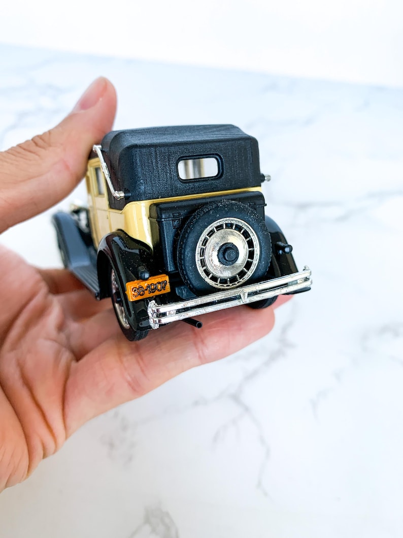 May include: A black and cream toy car model with a black convertible top. The car has a license plate that reads "33-1007".