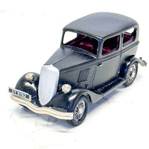 May include: A black vintage toy car with a silver front grill and headlights. The car has a license plate that reads "EV 9762". The interior of the car is a deep red color. The car has four wheels and a rounded roof.