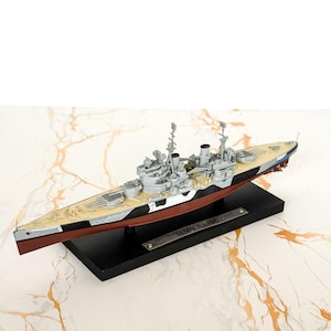 May include: A scale model of the battleship HMS Anson featuring a red hull, a black and white camouflage pattern on the sides, and a tan deck. The model is mounted on a rectangular black display base with a metal plaque labeled HMS Anson.