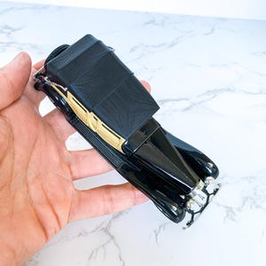 May include: Black and gold vintage toy car model with a black fabric top. The car has a detailed front grill and chrome accents.