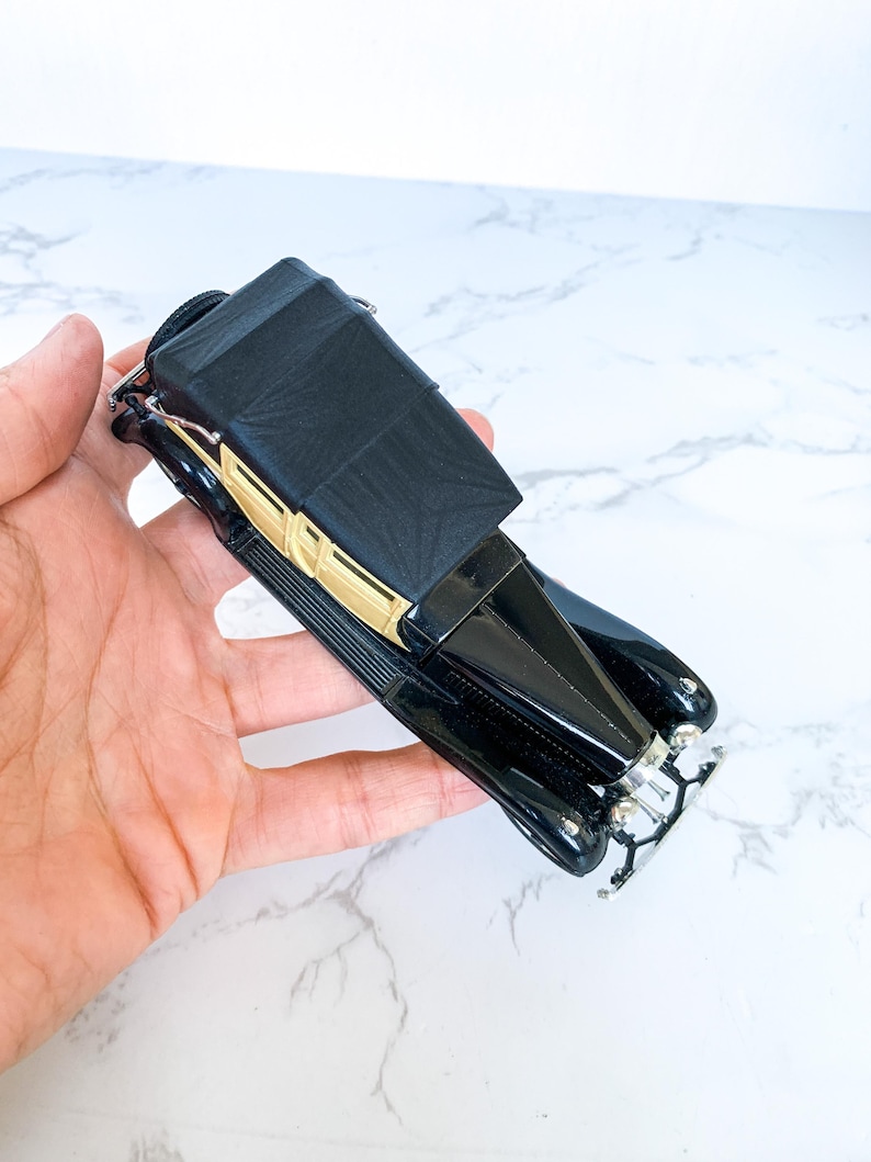 May include: Black and gold vintage toy car model with a black fabric top. The car has a detailed front grill and chrome accents.