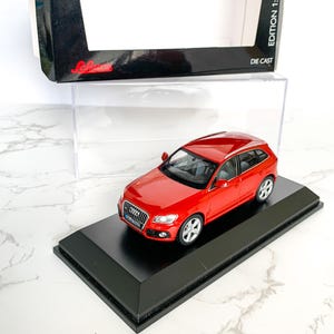 May include: Red die-cast model car of an Audi Q5 in a clear display case on a black base. The box is labeled "Die Cast Edition 1:43".