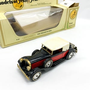 May include: A black and red toy car with a white roof. The car is a 1930s Packard and is part of the Matchbox Models of Yesteryear series. The car is in its original box.