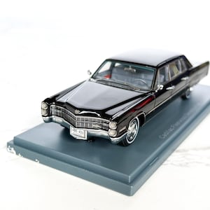 Puede incluir: Un coche de juguete Cadillac Fleetwood negro con detalles cromados, expuesto sobre una base gris. El coche modelo tiene una parrilla delantera detallada, faros y una placa de matrícula que dice HBG 400. Es un modelo de coche clásico vintage.