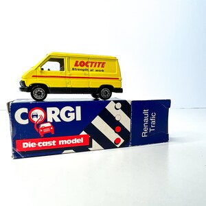 Puede incluir: Una furgoneta de juguete amarilla de metal fundido a presión con las palabras "Loctite Strength at work" en el lateral. La furgoneta está sobre una caja azul y blanca con las palabras "Corgi die-cast model" y "Renault Traffic".