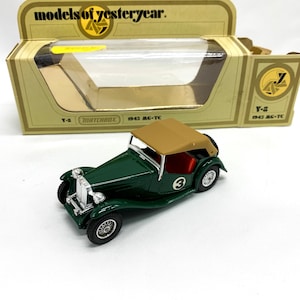 Może przedstawiać: Zielony model samochodu Matchbox przedstawiający MG-TC z 1943 roku, z beżowym składanym dachem i numerem "3" na boku. Samochód znajduje się w żółto-brązowym pudełku z napisem "models of yesteryear" na górze.
