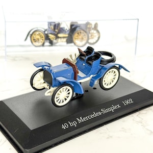 May include: A blue 1902 Mercedes-Simplex model car with white spoked wheels and a black base. The model car has a brown steering wheel and black seats. The text "40 hp Mercedes-Simplex 1902" is printed on the base.