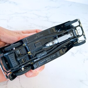 May include: Black diecast model car of a Bugatti Royale 41 1050, with the words "BUGATTI ROYALE 41 1050" and "1/18" printed on the bottom. The car is made in Italy by RIO.