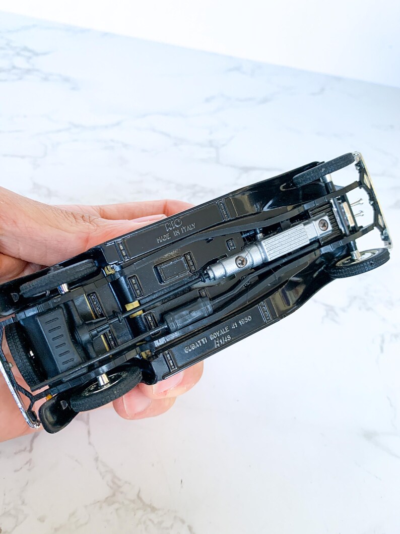 May include: Black diecast model car of a Bugatti Royale 41 1050, with the words "BUGATTI ROYALE 41 1050" and "1/18" printed on the bottom. The car is made in Italy by RIO.