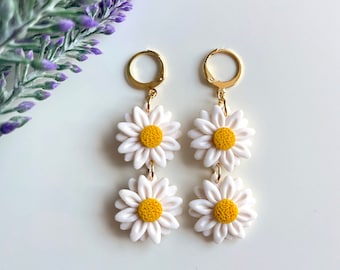 May include: A pair of gold dangle earrings with three white daisy flower charms. The daisies have yellow centers.