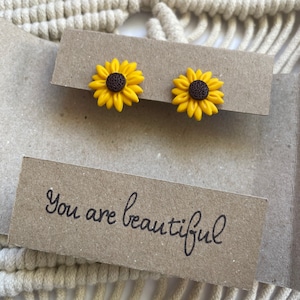 Könnte beinhalten: Ein Paar gelbe Sonnenblumenohrringe auf einer braunen Karte mit dem Text "You are beautiful".