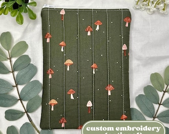 Pode incluir: Uma bolsa verde acolchoada com um padrão repetido de cogumelos laranja e brancos. A bolsa tem um zíper branco e o texto "custom embroidery (optional)" em um oval branco.