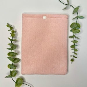 Puede incluir: Una funda de libro de pana rosa con cierre de botón blanco.