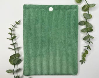 May include: A green corduroy book sleeve with a white button closure.