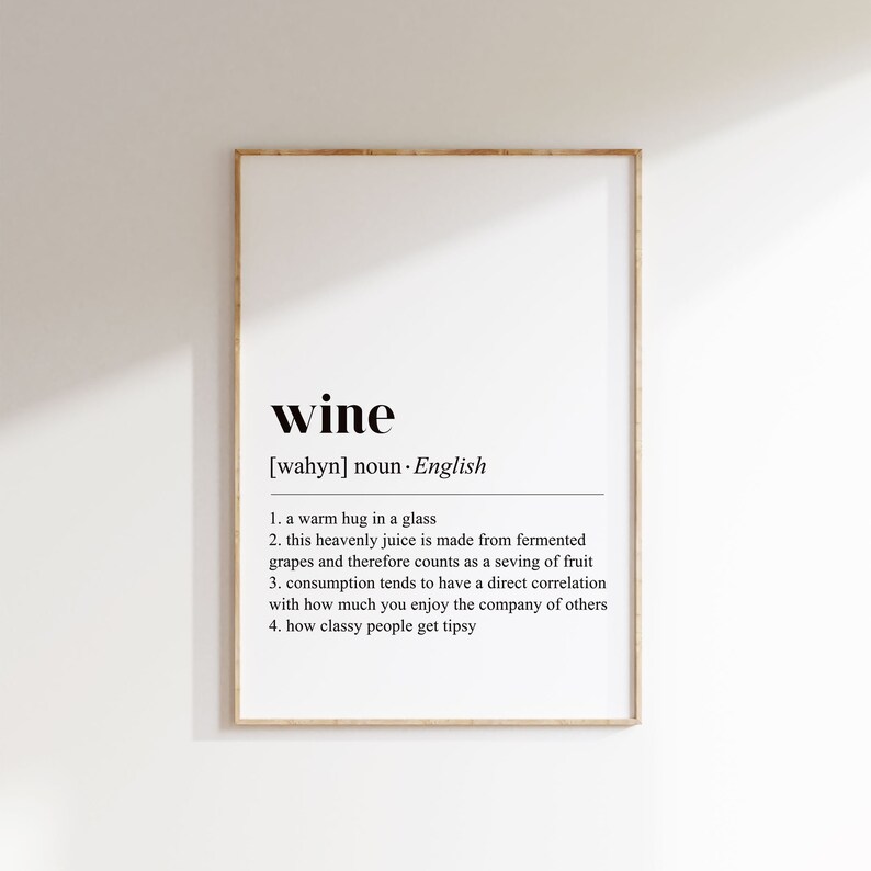 Op de afbeelding: Een ingelijste print met de definitie van "wine" in zwarte tekst op een witte achtergrond. De definitie bevat de uitspraak, woordsoort en vier beschrijvende uitspraken over wijn.