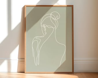 May include: A framed art print featuring a minimalist line drawing of a person's back and head, with their hair in a bun. The artwork is rendered in white lines against a muted green background. The frame is made of light-colored wood.