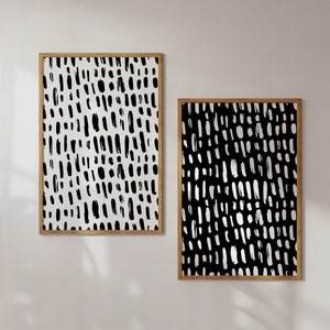 Puede incluir: Dos impresiones art&iacute;sticas abstractas enmarcadas. Una impresi&oacute;n presenta un fondo blanco con trazos de pincel negros, y la otra tiene un fondo negro con trazos blancos. Ambas est&aacute;n en marcos de madera.