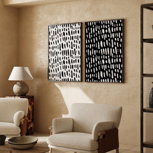 Puede incluir: Dos impresiones art&iacute;sticas abstractas enmarcadas. Cada impresi&oacute;n presenta un patr&oacute;n en blanco y negro de pinceladas verticales. Los marcos son negros. El arte se exhibe en una habitaci&oacute;n con muebles y decoraci&oacute;n de tonos neutros.