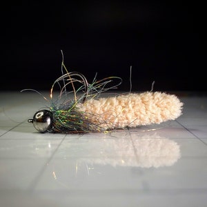 May include: A tan and green fly fishing lure with a fluffy body and a silver bead head.