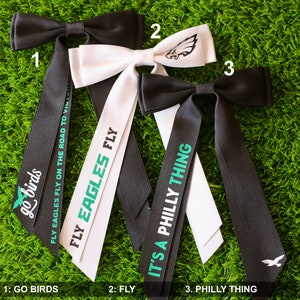 May include: Three black and white bow ties with green text. The first bow tie has the text "go birds" on it. The second bow tie has the text "FLY EAGLES FLY" on it. The third bow tie has the text "IT'S A PHILLY THING" on it.